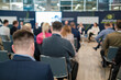 Focused shot of attendees at a business conference. The discussion panel is blurred in the background, highlighting engagement and learning.