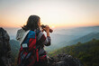Female tourist on top of mountain use binoculars to view mountain range at sunset