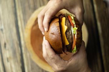 Duas mãos segurando um hamburguer em cima de uma mesa de madeira Two hands holding a burger on a wooden table 11