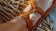 Close-up of a woven leather sandal, showcasing a playful seashell charm and tanned toes peeking through the straps