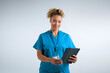 Studio Portrait Of Smiling Female Nurse Wearing Scrubs With Digital Tablet Against Grey Background