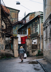 Wall Mural - Old lady walking in the street of Tbilisi old town (Georgia), surrounded by dilapidated houses