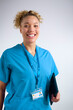Studio Portrait Of Smiling Female Nurse Wearing Scrubs With Digital Tablet Against Grey Background