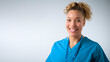 Studio Portrait Of Smiling Female Nurse Wearing Uniform With Security Lanyard On Grey Background