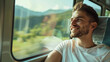 A man is smiling and looking out the window of a train