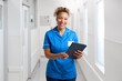 Portrait Of Smiling Female Nurse Wearing Uniform In Hospital Corridor With Digital Tablet