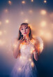 Portrait of a beautiful Asian woman with angelic wings, wearing white clothes and illuminated by the glow of a garland, exuding beauty and elegance.