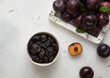 Sweet prunes in glass bowl with ripe plums in wooden box on light kitchen background.Top view.