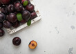 Wooden box of raw ripe purple plums on light kitchen background.Top view.
