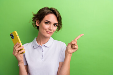Photo of young advertiser girl pointing finger empty space to show you new application using smartphone isolated on green color background
