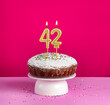 Birthday cake with number 42 candle on pink background