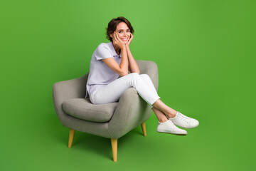 Poster - Full length photo of funky dreamy girl dressed grey polo sitting chair arms cheeks empty space isolated green color background