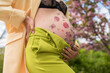 belly of pregnant girl close-up with hand with floral ornament, bright clothes, spring vibe