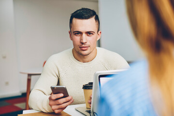 Wall Mural - Portrait of serious candidate for vacancy looking at camera checking mail with online letter sitting in office during interview,male worker looking at camera chatting via smartphone on coffee break