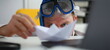 Man wearing suit and tie in goggles and snorkel play with paper ship in office portrait. Count days to leave annual day off workaholic freedom fun tourism resort idea ticket sale concept