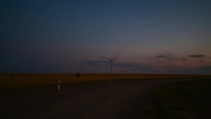 Wall Mural - Side view of silhouettes of wind turbines in wind farm rotating and working at twilight. Some clouds on sky. Real time handheld video. Renewable electricity generation theme.