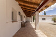 Covered porch with wooden roof of an Andalusian style country house with terracotta sidewalks, wooden benches, white walls, gravel path, a newly planted olive tree on a bright and pleasant day