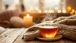 © Jinny787 - A cup of steaming tea on a wooden table. The tea is surrounded by a cozy scarf and there is a candle in the background. The mood is warm and inviting.