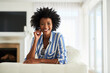© peopleimages.com - Portrait, black woman and couch in home for relax, calm or living room on break. Face, smile or rest on sofa in lounge for female person with afro, furniture or peace on weekend for wellness in house