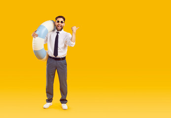 Full body photo of excited funny young man in summer sunglasses and holding rubber ring in office clothes pointing index finger to the side to copy space isolated on yellow studio background.