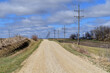 A unpaved country road stretches to the horizon on a sun-drenched late winter day in rural Illinois. The empty roadway sees very little traffic being used predominantly by farm residents in the area.