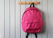 pink school backpack hangs on a wooden hanger on a white board wall. Copy space. concept: no plastic. natural interior.