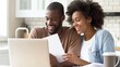 © lililia - a young couple seated together at a kitchen table, their radiant smiles illuminating the room as they joyfully review documents on a laptop.