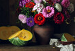 a dark still life with flowers and pieces of pumpkin.