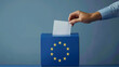 A person entering a vote into a ballot box European Union flag in background. European elections