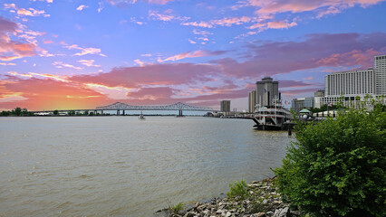 a gorgeous spring landscape along the MIssissippi River with boats sailing and the Crescent City Connection bridge with hotels and office buildings in the city skyline n New Orleans Louisiana USA