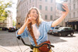 Young woman using mobile phone while  riding bicycle at the city street outdoor. Telecommunications, video call conference, communication with friends and family remotely. Selfie time.