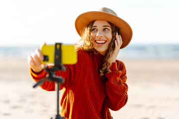Wall Mural - Style woman using smartphone with stabilizer, taking pictures and live video on the seashore. Travel, technology concept.
