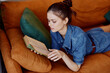 Young woman in denim shirt reading book on orange couch in cozy living room setting