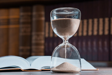 Hourglass and opened book on library table