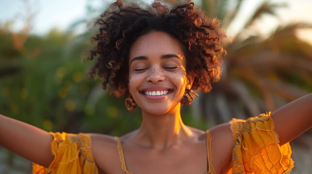 A joyful woman with curly hair smiling with her arms outstretched against a soft-focus natural background.