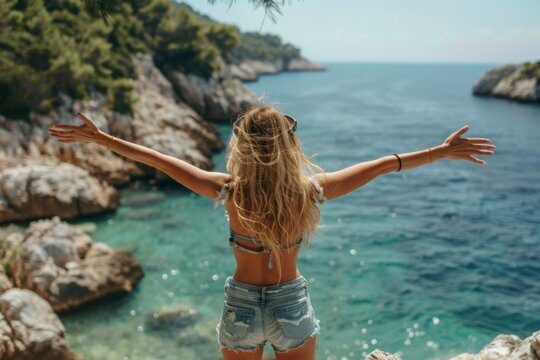 woman standing on rocks overlooking the sea in croatia, arms outstretched, enjoying nature