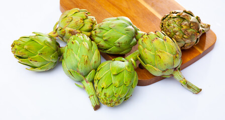 Wall Mural - Pile of fresh ripe artichokes on wooden cutting board on white background. Organic vegetarian food concept..