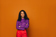 © Jacob Lund - Thoughtful woman with curly hair standing on vibrant orange background, arms crossed and smiling