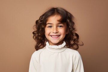 A young girl with curly hair is smiling and wearing a white shirt