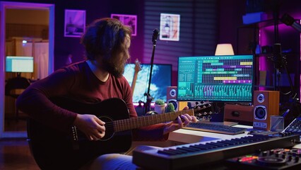 Poster - Portrait of male songwriter playing acoustic guitar and recording musical sounds to use for mix and master in home studio. Composing tunes with digital audio workstation software. Camera B.