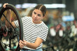 Glad young girl selects bicycle in modern sporting goods store, checking wheel quality