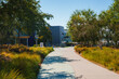 Sunny day at modern campus with curving pathway among well maintained landscaping. Building with number 43 stands out in blue and gray. Simultaneously peaceful and pristine atmosphere.