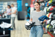 Positive female customer choosing safe bicycle helmet in modern sports bike store