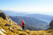 A tourist in a bright jacket, photographed from the back, walks along a mountain path against the backdrop of the sea coast. A man goes hiking in the municipality of Herceg Novi, Montenegro