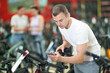 Young guy using smartphone for examining quality seat and choosing bike in modern bicycle sports store