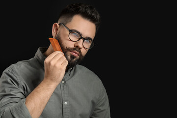 Canvas Print - Handsome young man combing beard on black background. Space for text