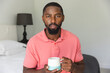 African American man holding mug, sitting indoors at home having a video call
