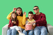 © Pixel-Shot - Little children with popcorn and their parents watching TV on sofa against green background