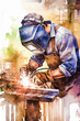 A welder, in full protective gear, is engrossed in his work. Sparks fly, creating a vivid display against a colorful, abstract backdrop