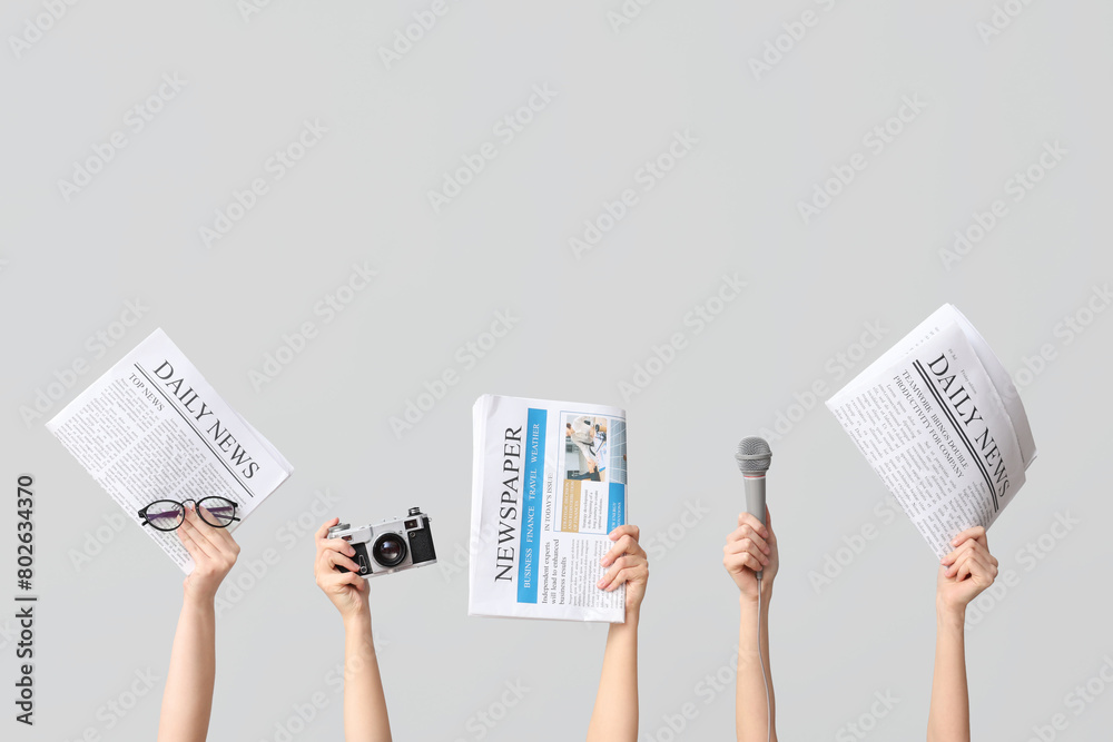 Female hands with newspapers, photo camera and microphone on grey background